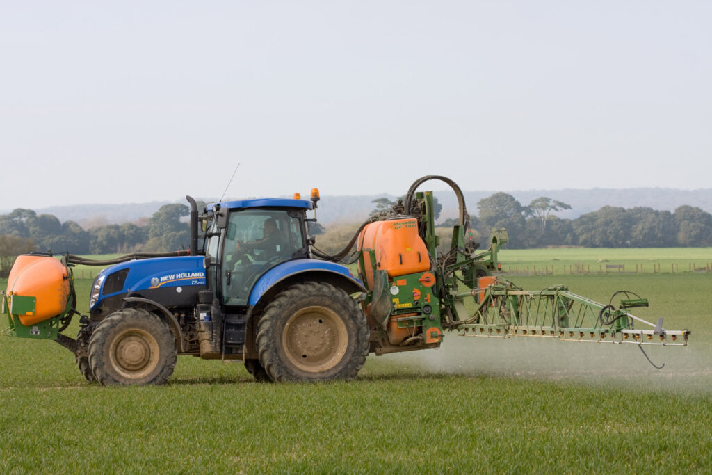 The image displays a tractor spraying fertilizers on a field